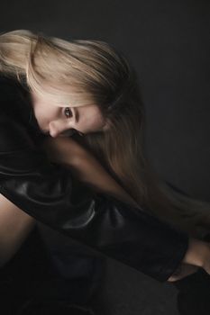 Artistic portrait of a woman in a black leather jacket, seated indoors.