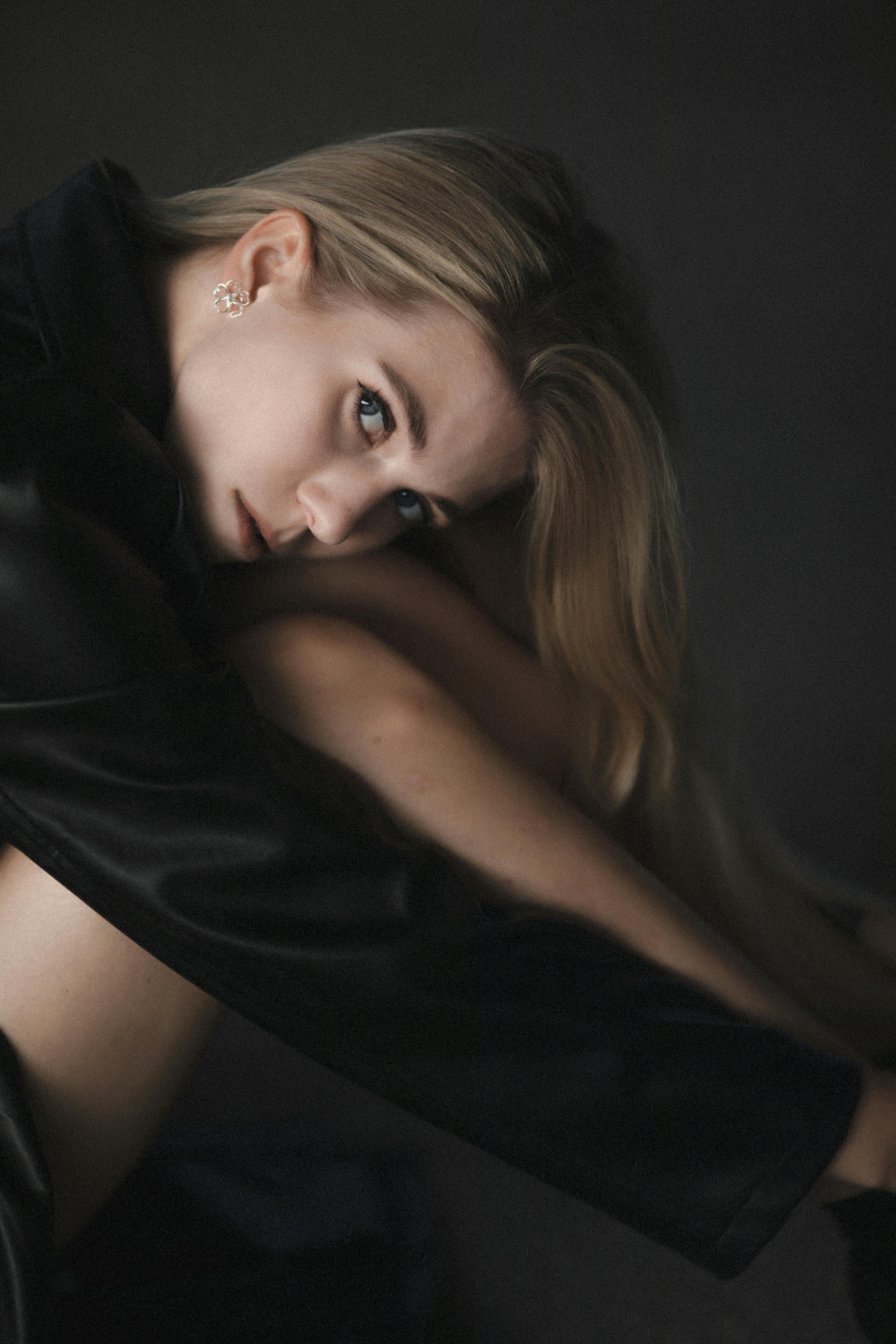 Captivating portrait of a blonde woman in a dark studio setting, exuding elegance and mystery.