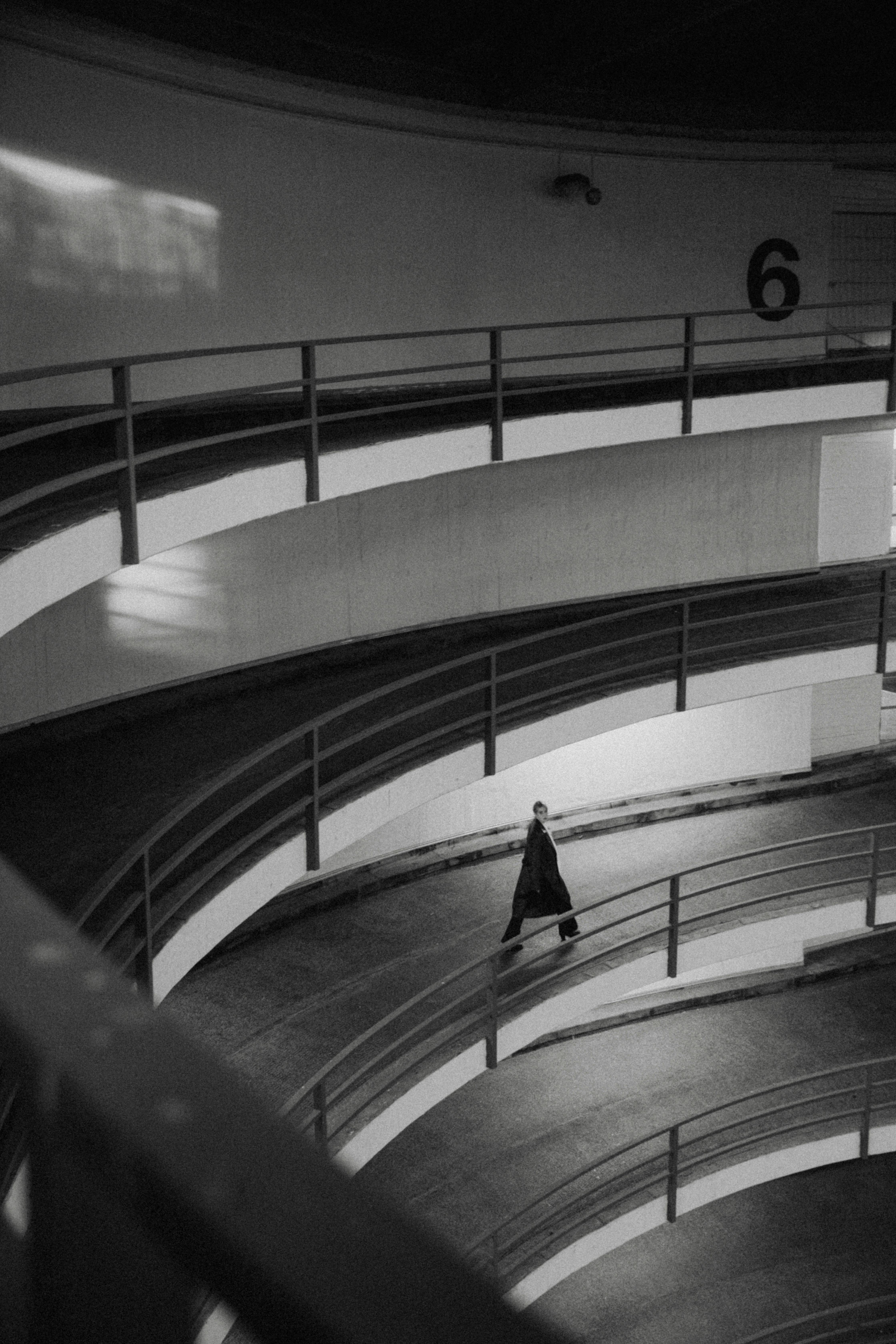 A woman walking alone in a modern urban parking garage in black and white.