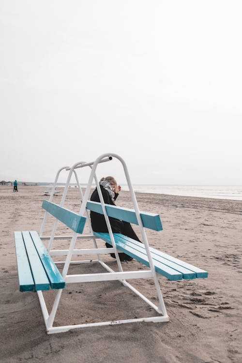 Woman Sitting on Bench on Beach on Cold Day