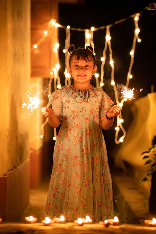 Free A joyful child holding sparklers, surrounded by lights during a night celebration. Stock Photo