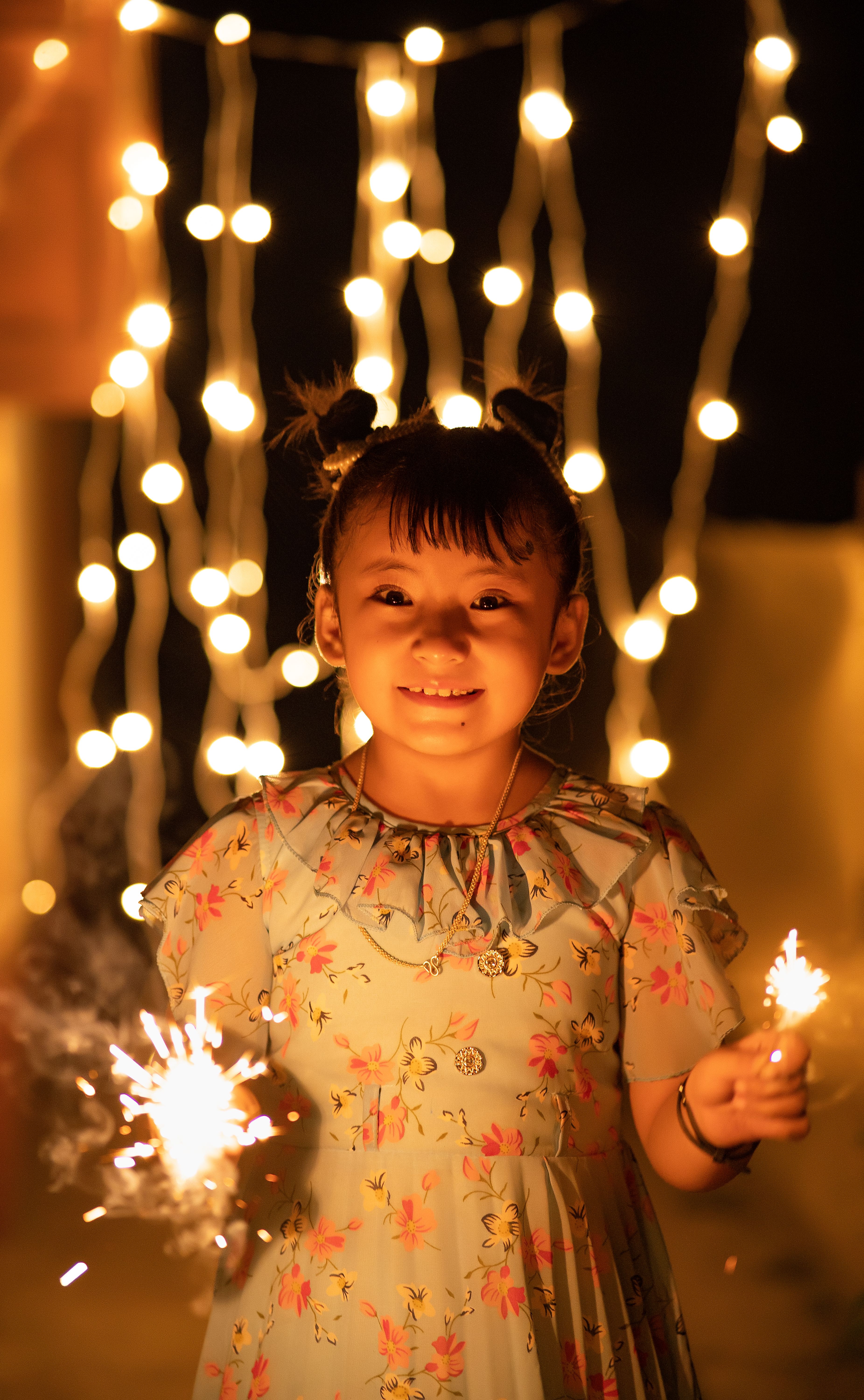 A smiling girl holds sparklers in front of festive lights, creating a joyful celebration atmosphere.