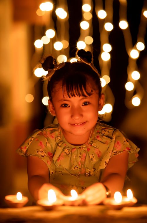 Free A young girl smiles warmly in candlelight, surrounded by glowing fairy lights. Stock Photo