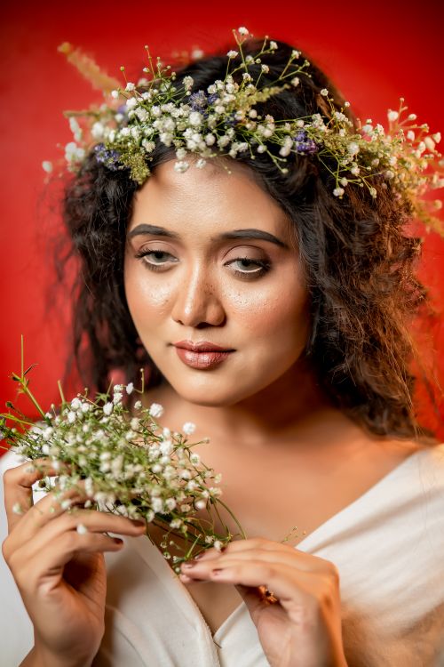 Free Portrait of a woman wearing a flower wreath, exuding elegance against a red backdrop. Stock Photo