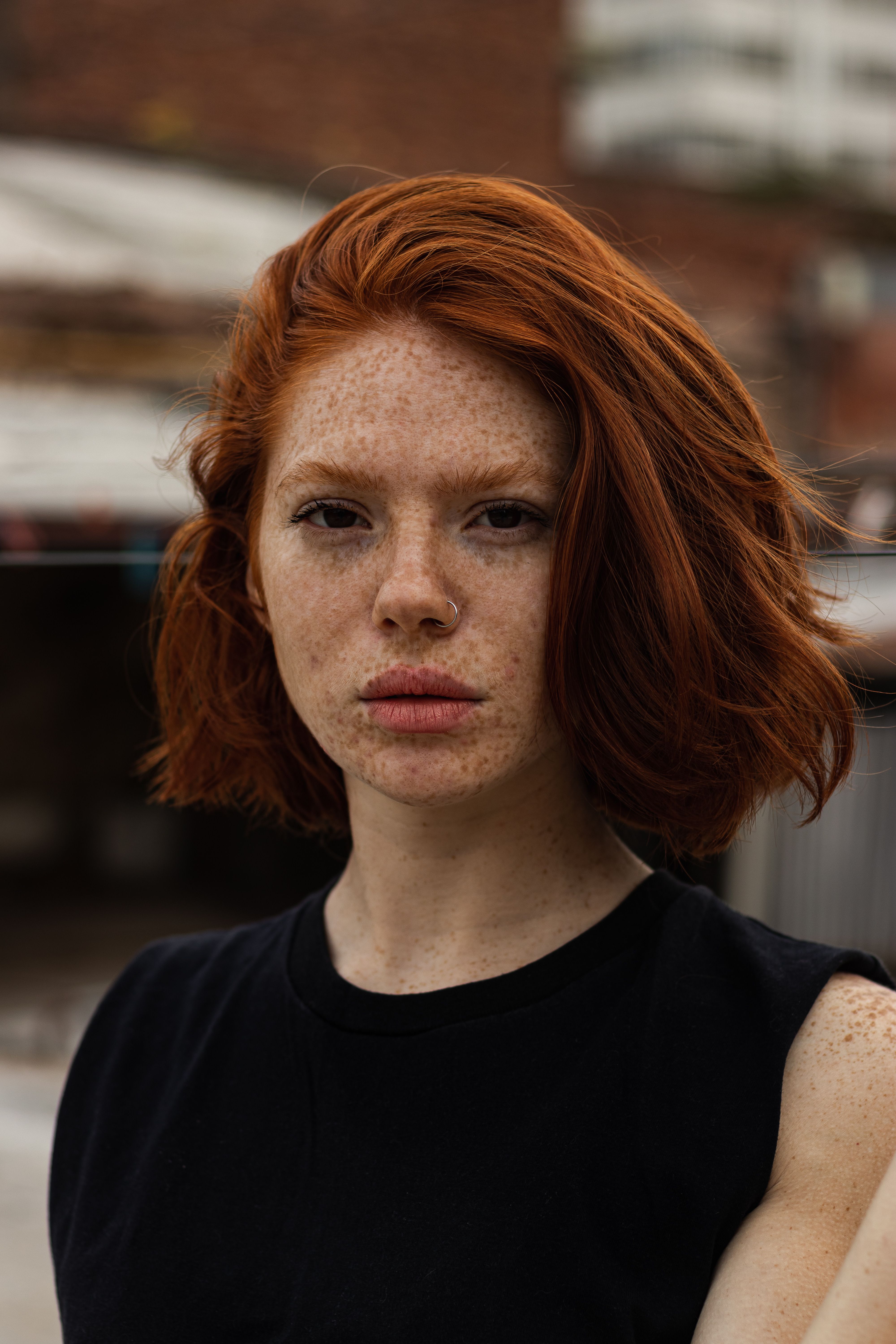 Portrait of a young redheaded woman with freckles and a nose ring, captured outdoors.