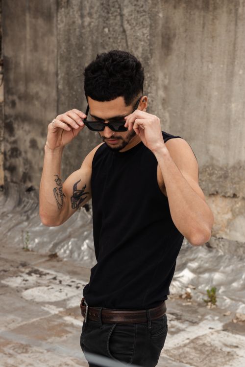 Free Fashionable man with tattoos adjusts his sunglasses outdoors, showcasing style and confidence. Stock Photo