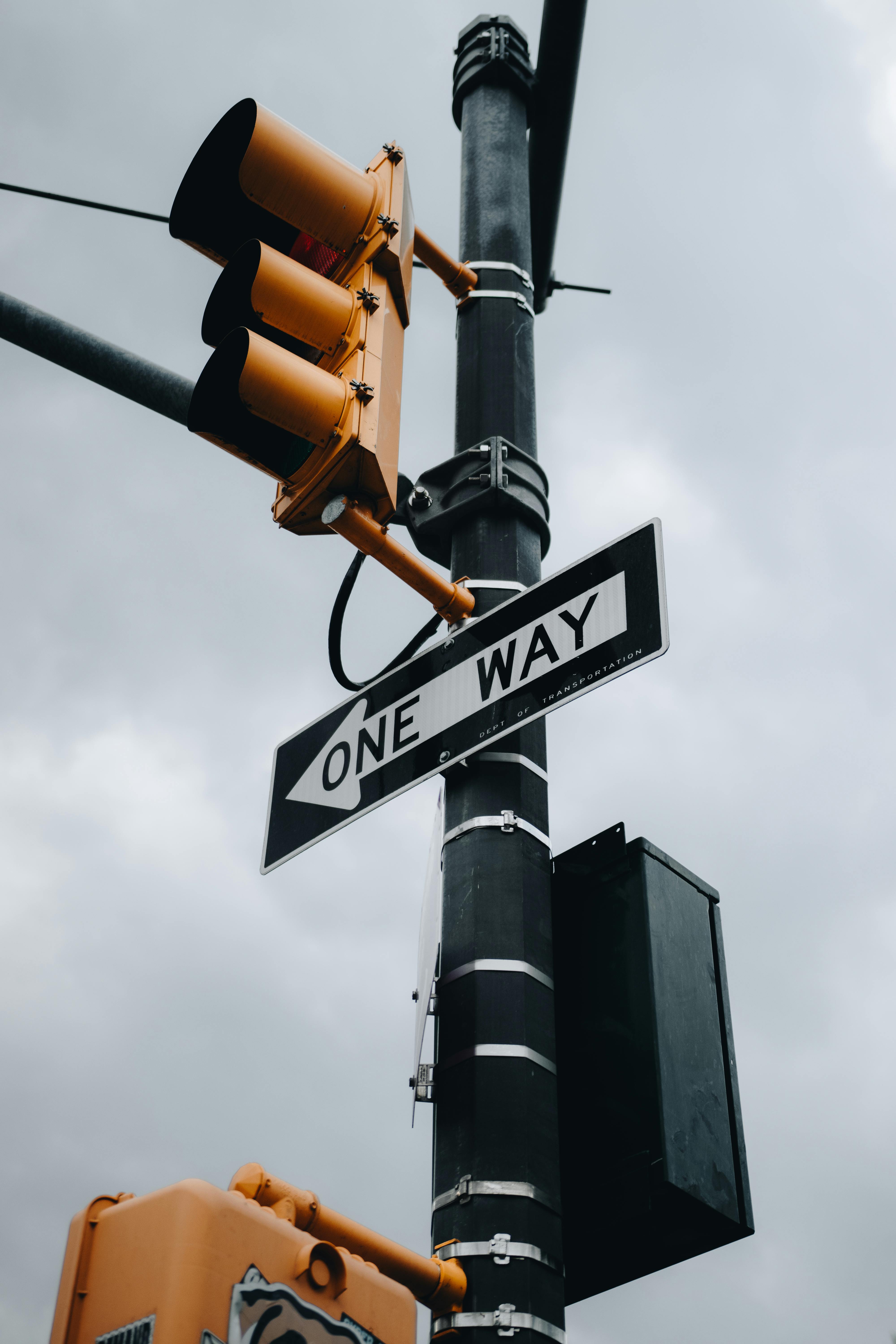 Close-up of a one-way sign and traffic light on a cloudy day in New York City.