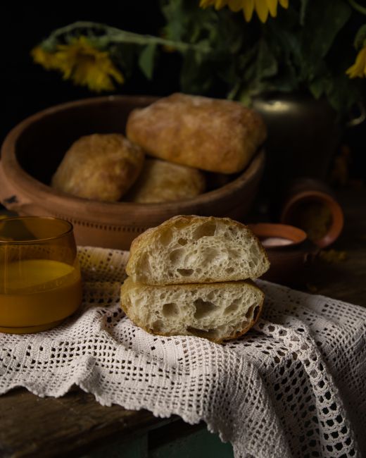 Several golden ciabatta rolls with an open, holey crumb, one sliced in half to show the airy interior and crisp crust.