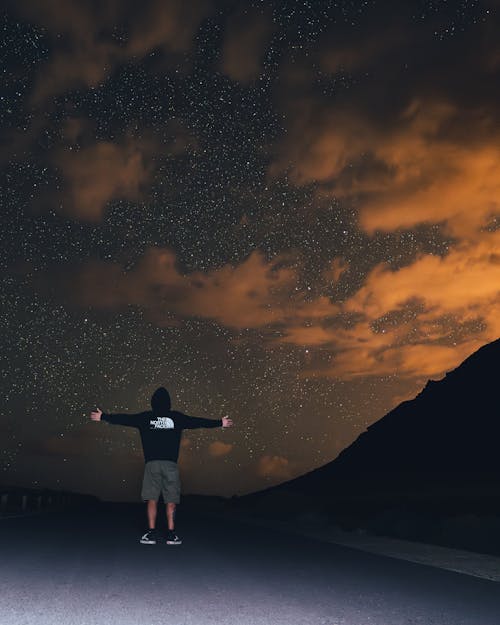 Back View of a Man Standing with Spread Arms under a Starry Night Sky 