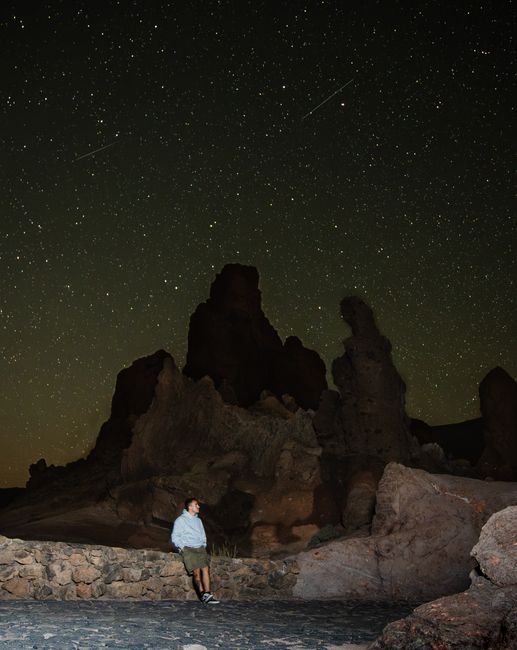 A man gazes at a star-filled sky amidst dramatic desert rock formations.