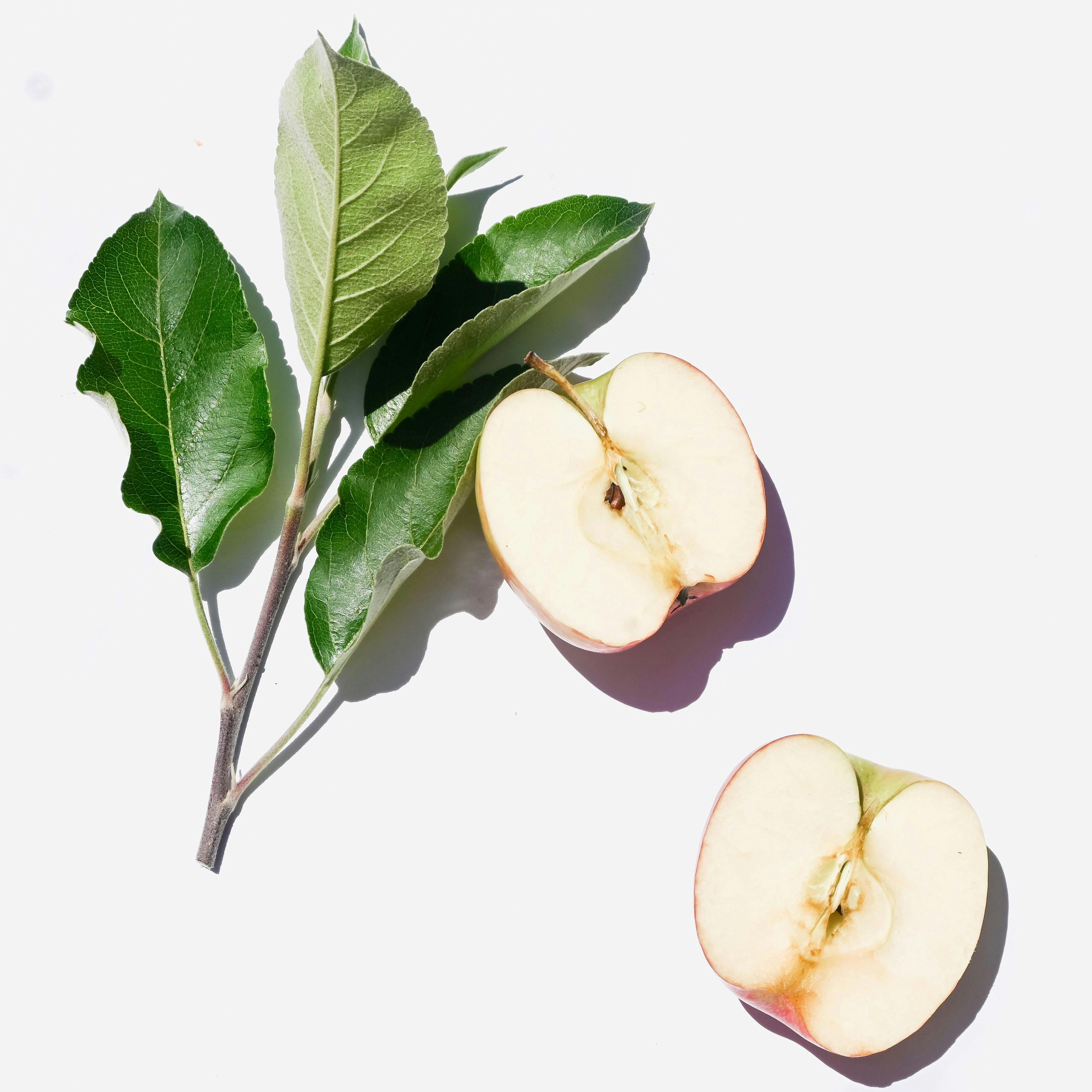 Crisp apple halves and green leaves on a white backdrop, showcasing freshness and simplicity.