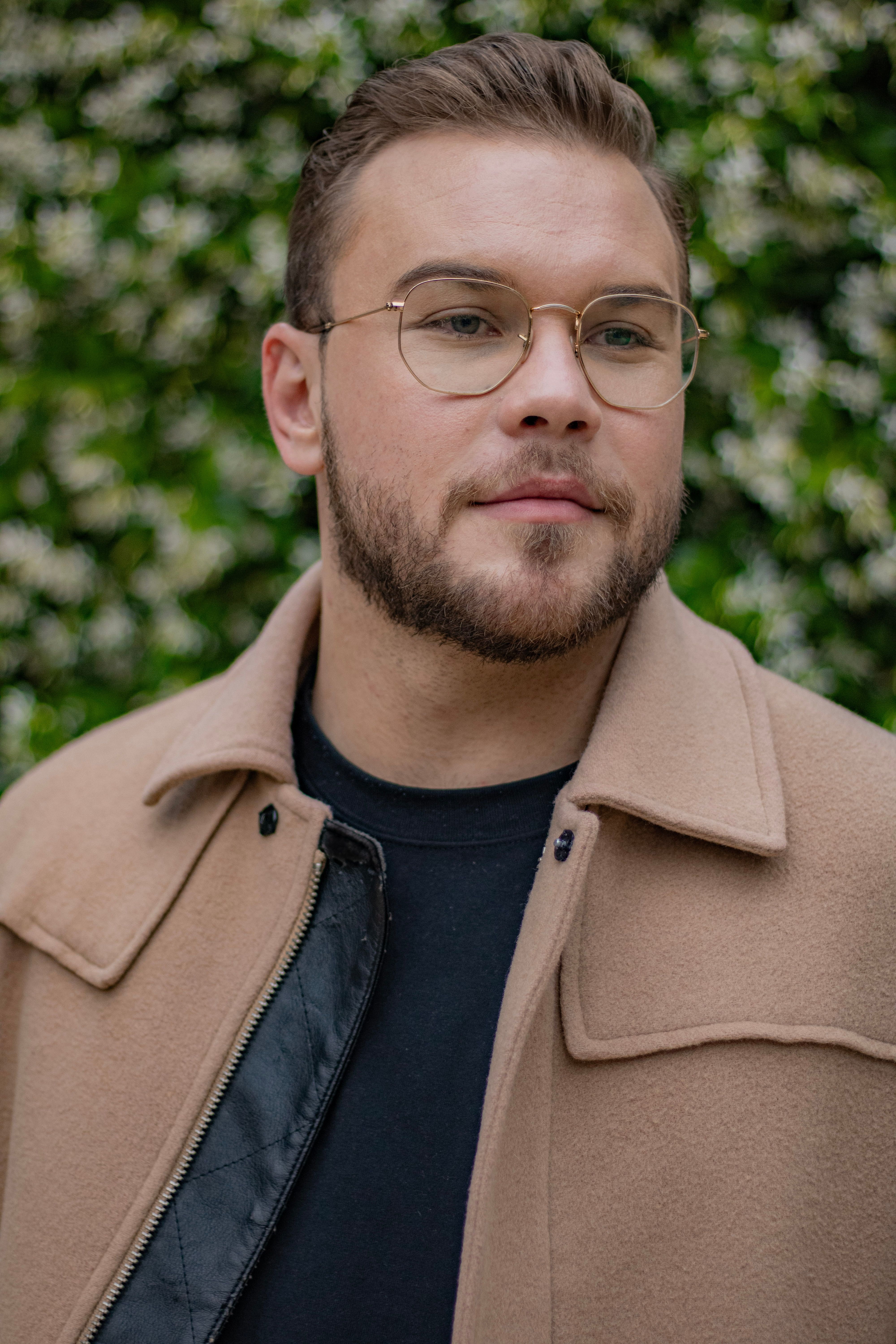 Portrait of a man wearing a beige jacket and eyeglasses, posing outdoors.