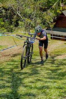 Male cyclist in Copacabana, Colombia, pushing mountain bike during race event outdoors on a sunny day.