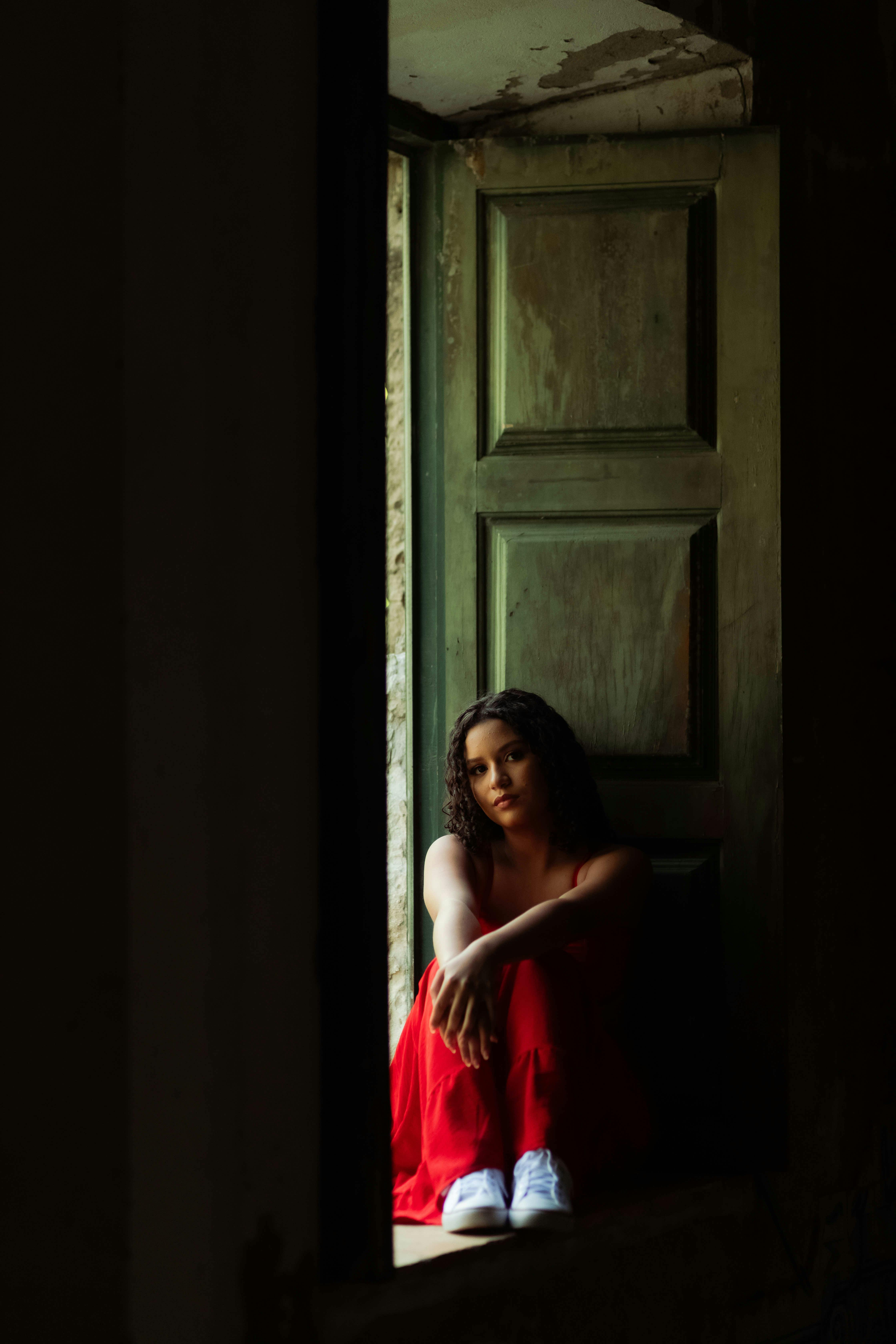 Dramatic shot of woman in a red dress sitting on a windowsill, Salvador, Brazil.