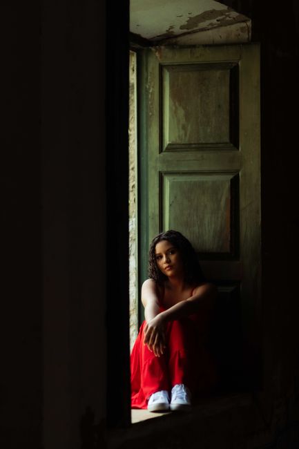 Dramatic shot of woman in a red dress sitting on a windowsill, Salvador, Brazil.