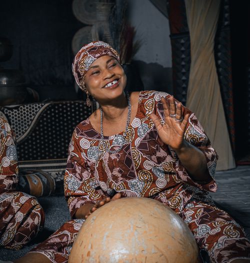 Free Smiling woman in traditional attire playing a drum indoors. Cultural expression of happiness. Stock Photo