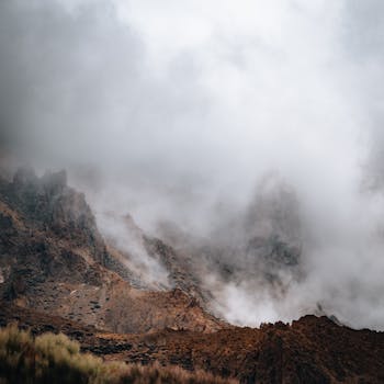 A dramatic landscape featuring rocky mountain sides shrouded in thick mist and fog.