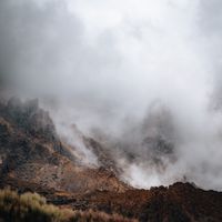 Album art: mist rolling over a rust-coloured mountain ridge — Martin Wischeropp on Pexels