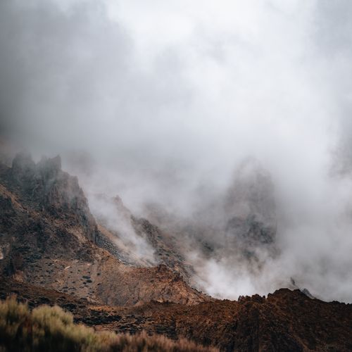 Album art: mist rolling over a rust-coloured mountain ridge — Martin Wischeropp on Pexels