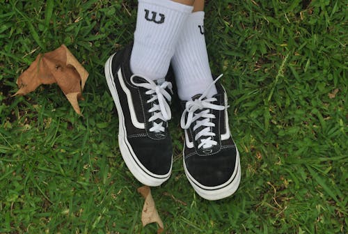 Close-up on Feet Wearing Black Vans Shoes on Green Grass