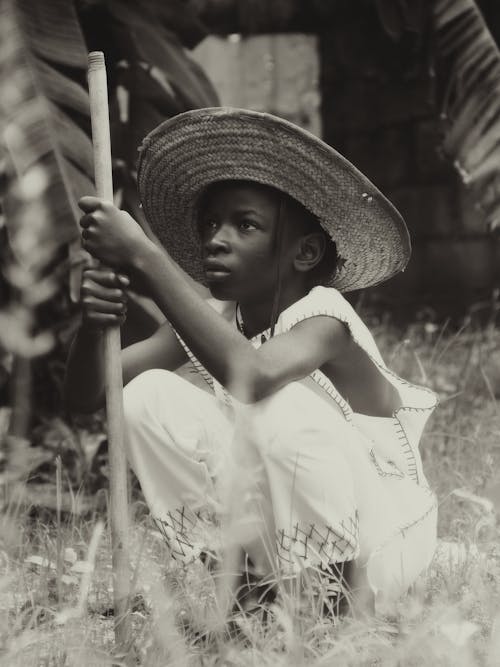 A Girl in a Hat Crouching on the Grass 