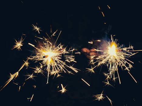 Hands holding sparklers creating a dazzling light display in a dark setting, perfect for festive celebrations.