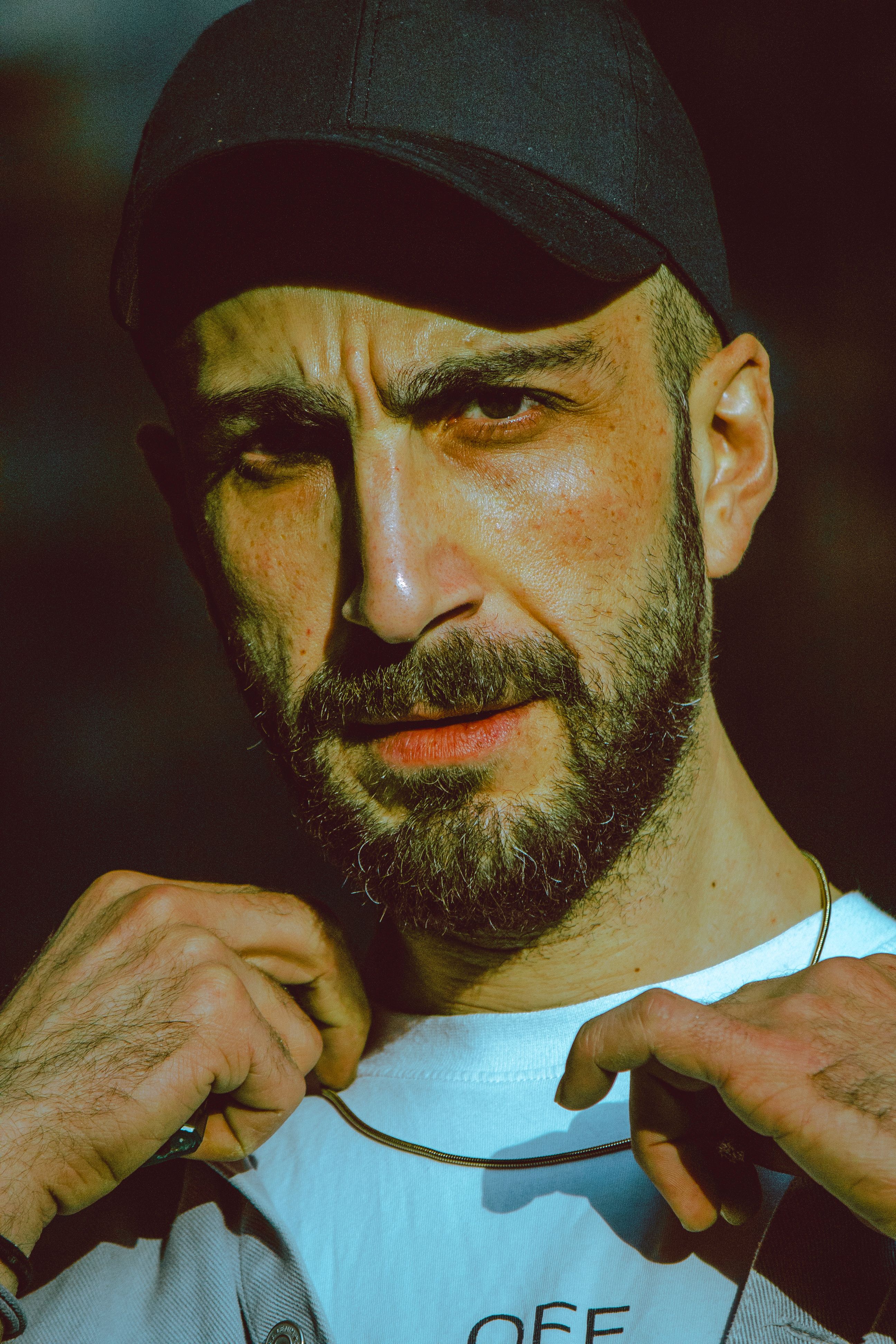 Close-up portrait of an adult man with a beard wearing a black cap in casual attire.