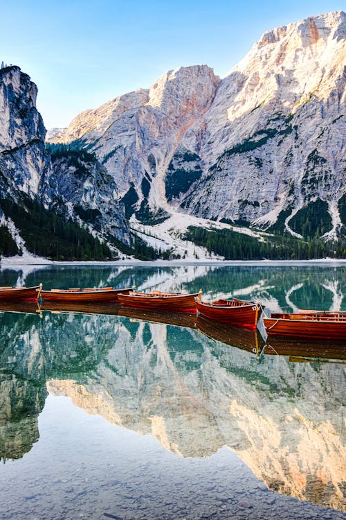 Row of Wooden Boats Tied Together on a Placid Lake Reflecting Mountains