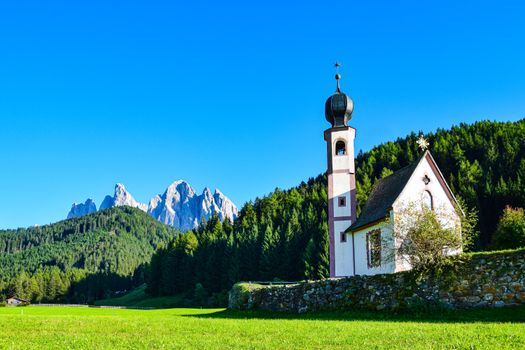 Picturesque church set against the dramatic Italian Alps, surrounded by lush forests.