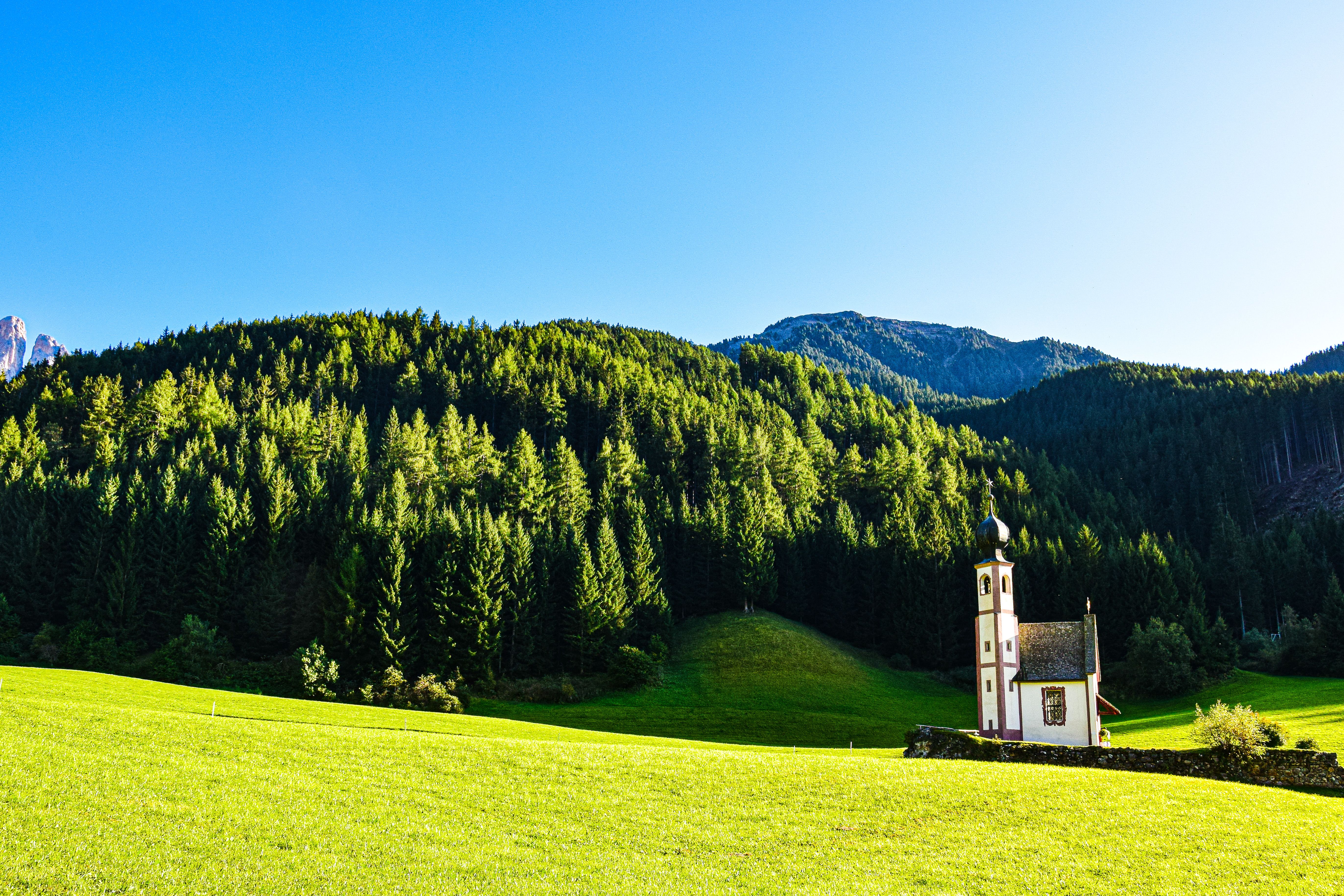 Sunlit church in Dolomites with forest and mountains, perfect travel scenery. Sunlit church in Dolomites with forest and mountains, perfect travel scenery.