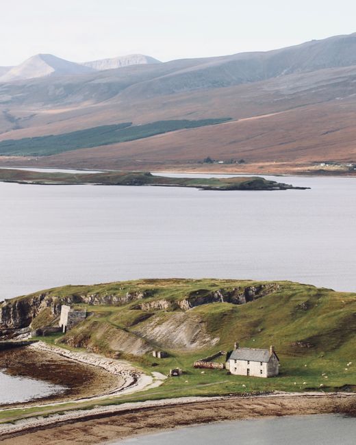 A picturesque rural landscape in Scotland featuring hills, a lake, and traditional stone buildings.