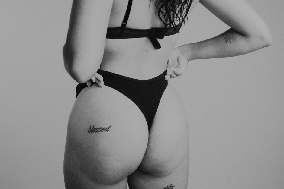 Artistic black and white photo of a woman in black lingerie with tattoos.