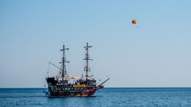 A pirate ship sails on open water with parasailing in the clear sky in Kemer.