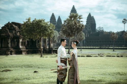 Free Elegant Khmer couple in traditional attire with Angkor Wat in the background, capturing a timeless wedding moment. Stock Photo