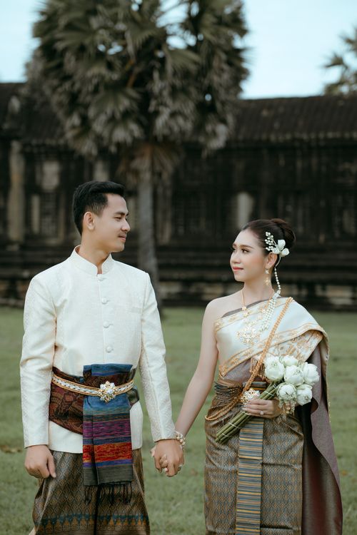 Free Traditional Cambodian couple in elegant wedding attire hold hands in a cultural setting. Stock Photo