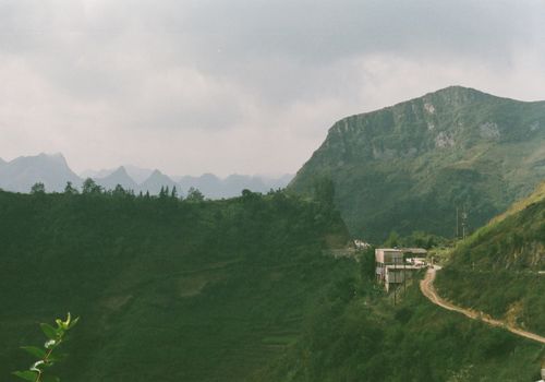 Free Aerial view of a tranquil rural village nestled in lush green mountains under a cloudy sky. Stock Photo