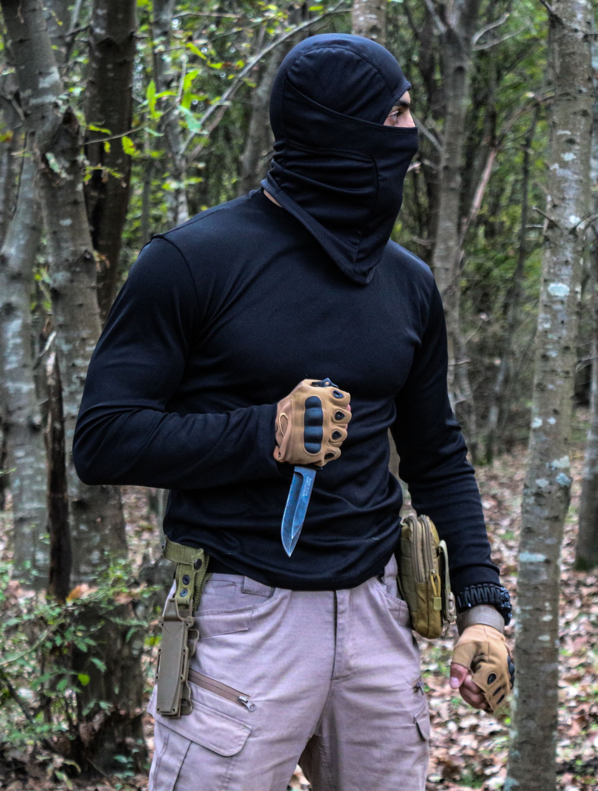 Masked fighter holding a combat knife in a shadowed forest setting