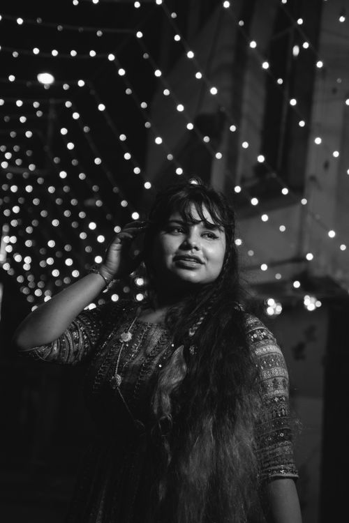 Free Black and white photo of a woman in traditional attire posing under festive lights at night. Stock Photo