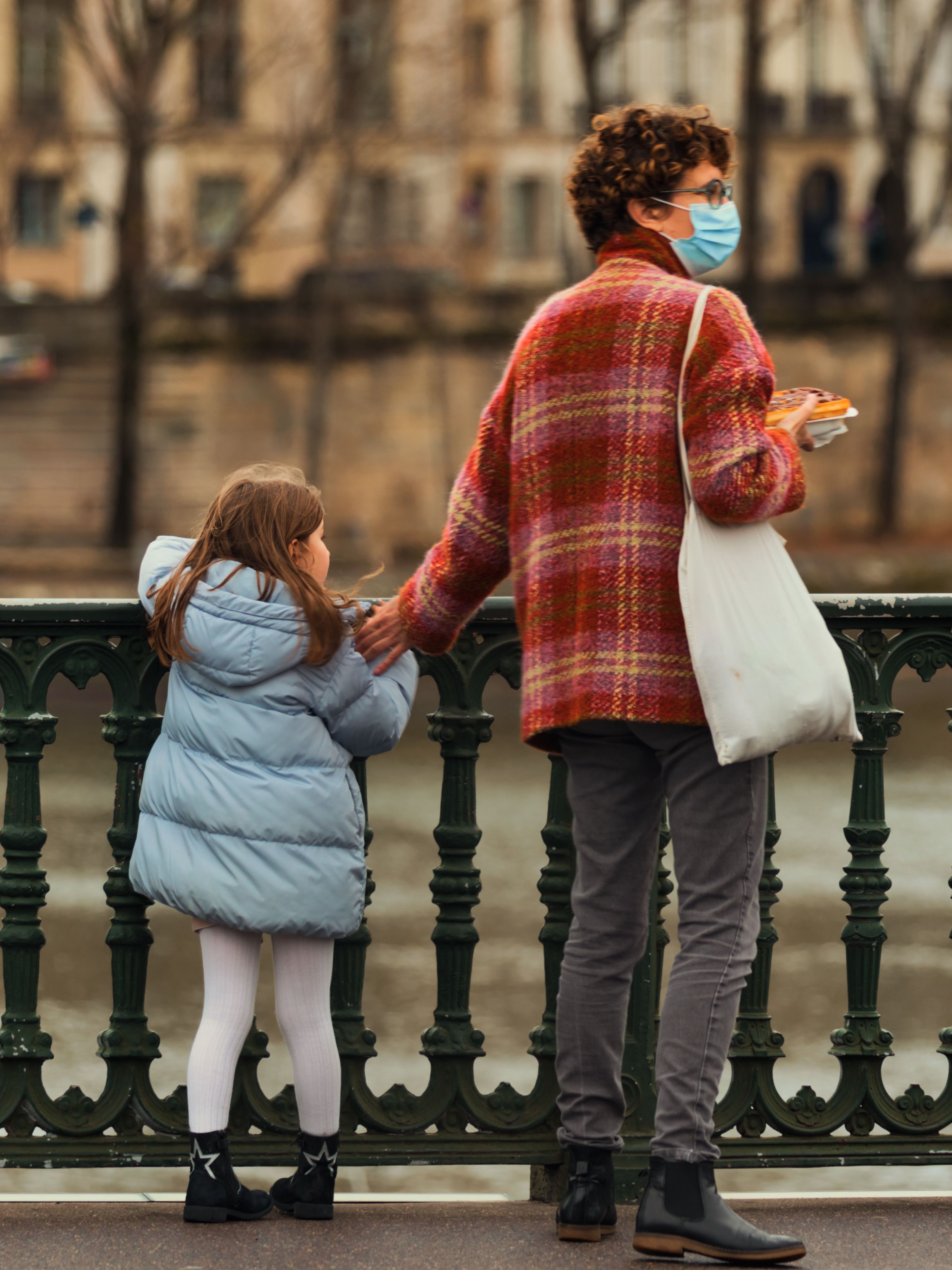 A mother and daughter walk on an urban bridge, wearing masks for protection in the fall season.