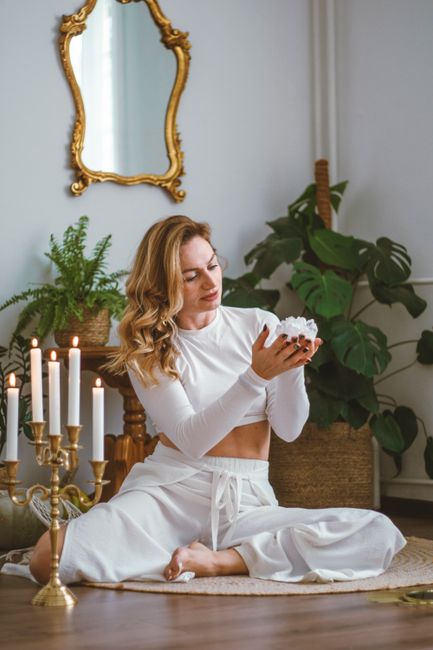 Woman meditating in a stylish living room with plants and candles, creating a peaceful atmosphere.