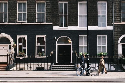 Free Street view of a person walking and another with a bicycle beside a dark brick residential building. Stock Photo