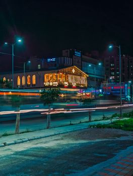 Illuminated street scene at night with modern architecture and light trails creating urban vibrancy.