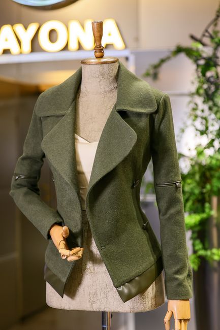 Elegant green coat displayed on a mannequin in a modern fashion store setting.