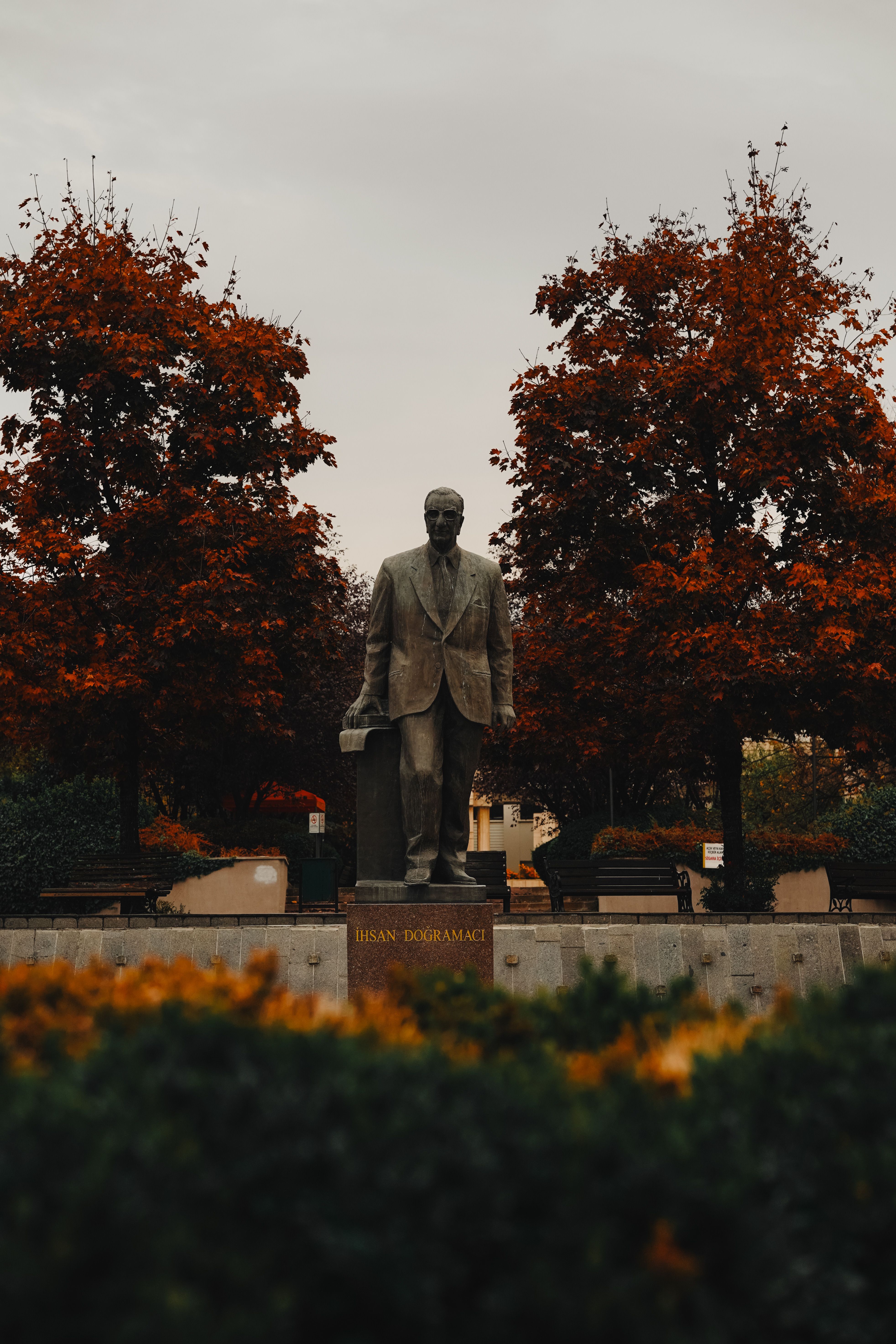 Serene autumn scene of Ihsan Dogramaci statue amidst vibrant trees in Ankara, Turkey.