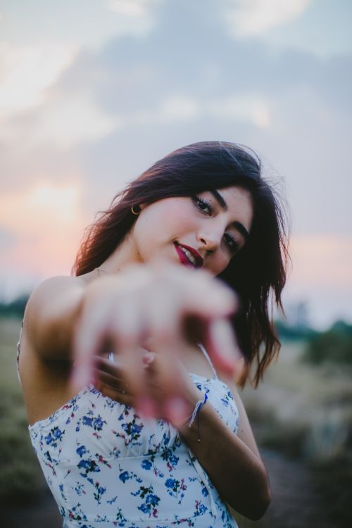 Free Charming young woman pointing with confidence during a serene sunset outdoors. Stock Photo