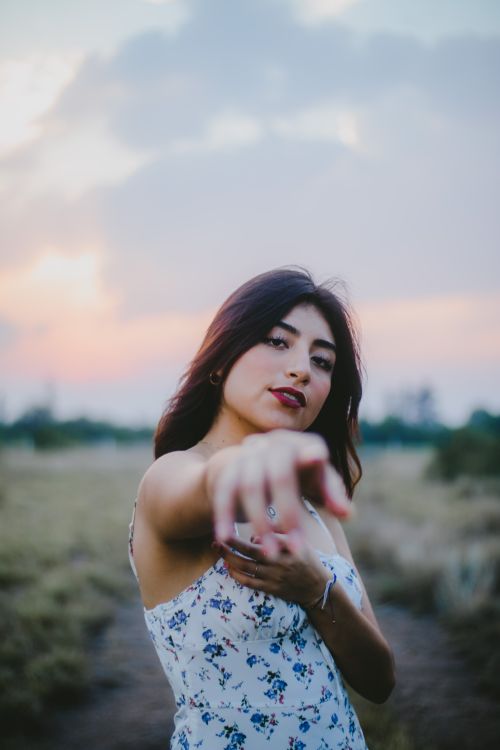 Free Trendy young woman in floral dress posing outdoors at sunset in a serene countryside setting. Stock Photo