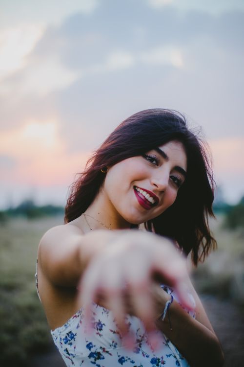 Free Cheerful brunette woman reaching out with a smile in a beautiful sunset field setting. Stock Photo
