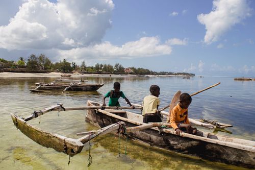 Free Boys paddling in traditional canoes on a sunny day in Zanzibar, Tanzania. Stock Photo