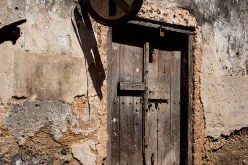 Free An old wooden door on a weathered stone wall, shadowed by a hand in Zanzibar, Tanzania. Stock Photo