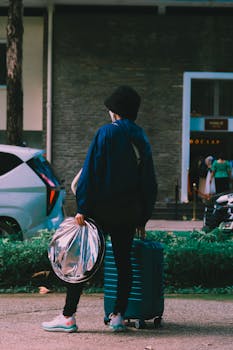 A woman traveler with suitcase and bag waiting on a city sidewalk.